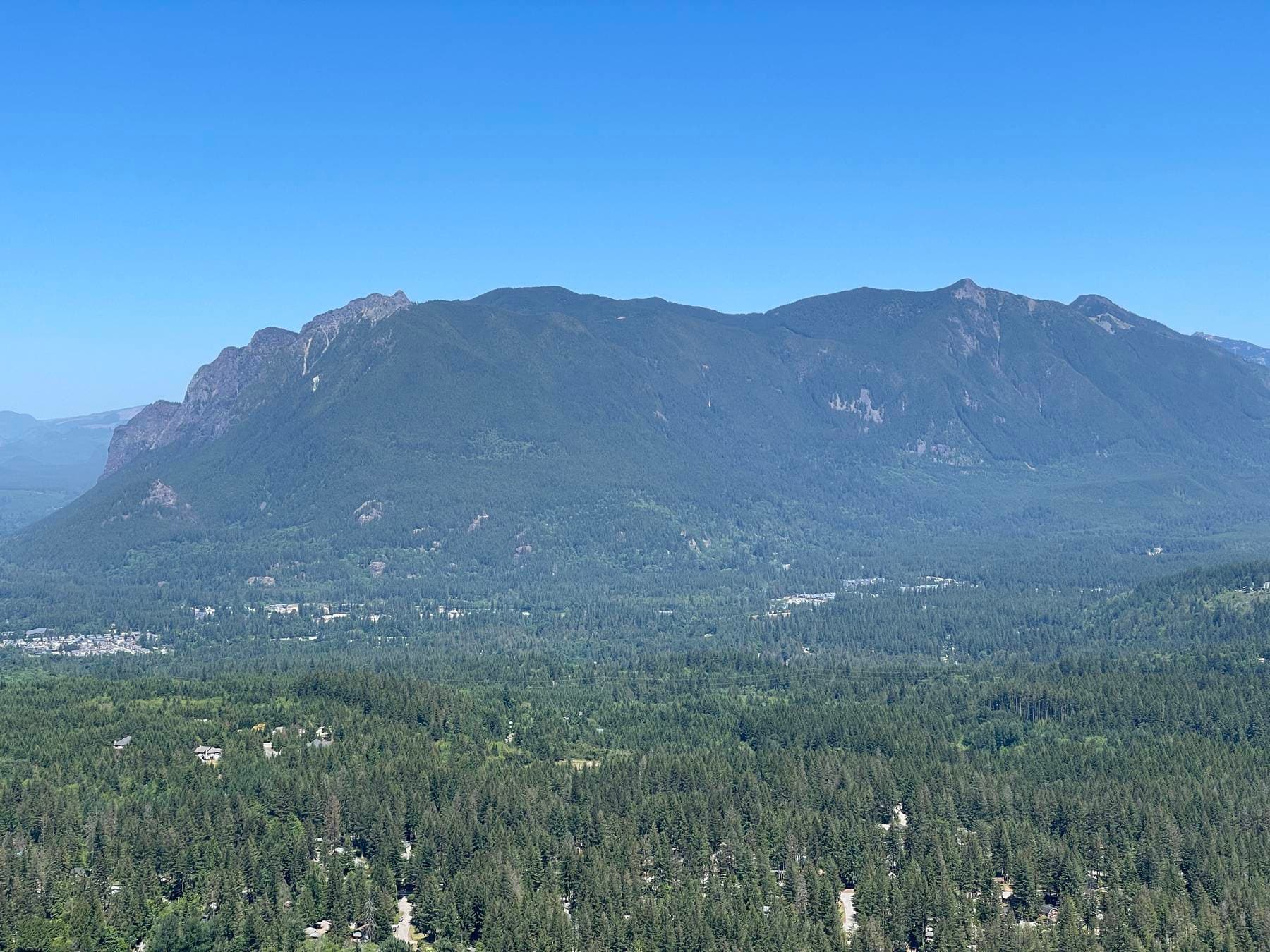 Forested Cascade foothills rising above the Snoqualmie Valley under a clear blue sky, seen from Rattlesnake Ledge