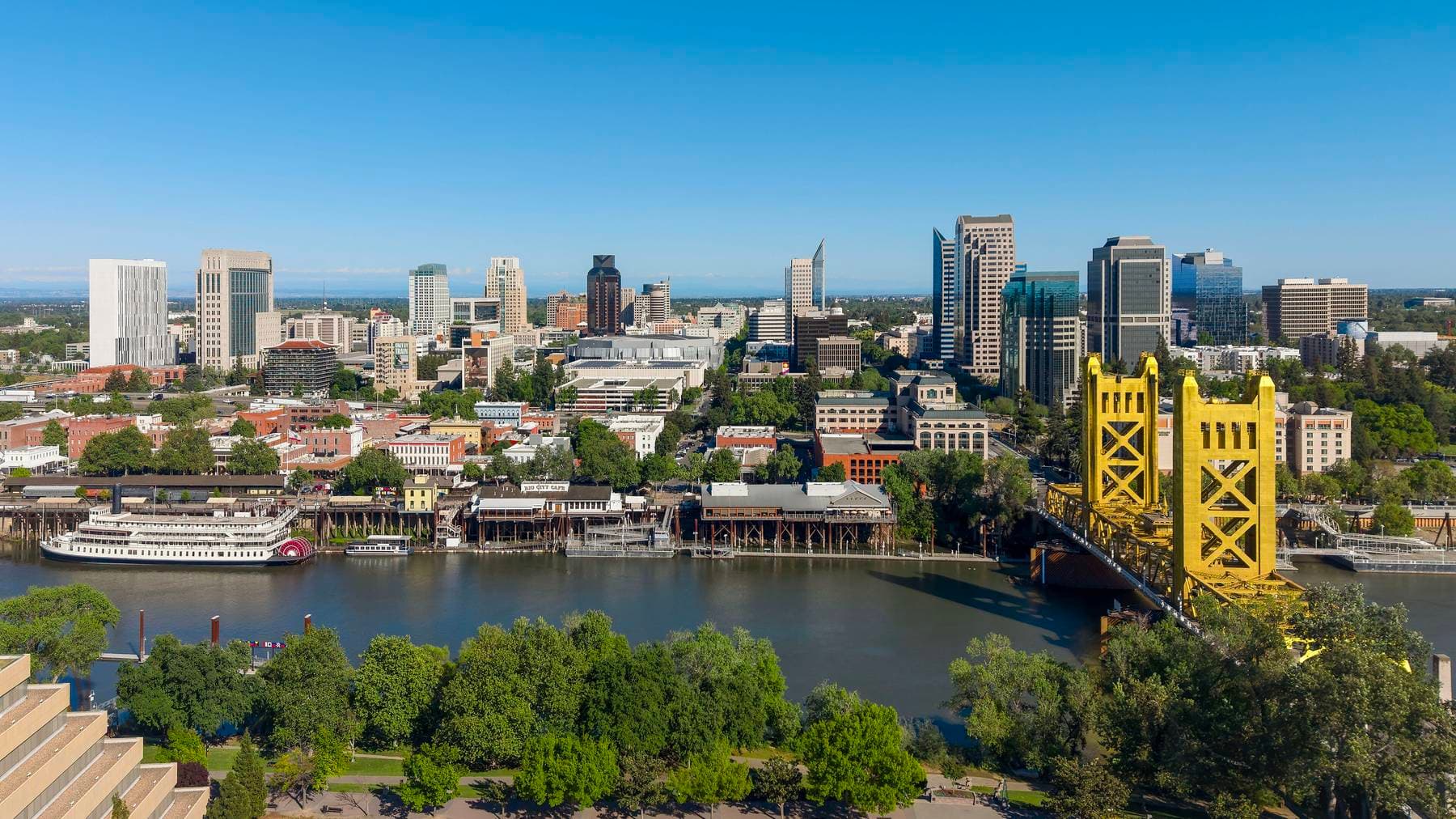 Downtown Sacramento skyline above the Old Sacramento waterfront, with a paddle-wheel riverboat and the gold Tower Bridge over the Sacramento River